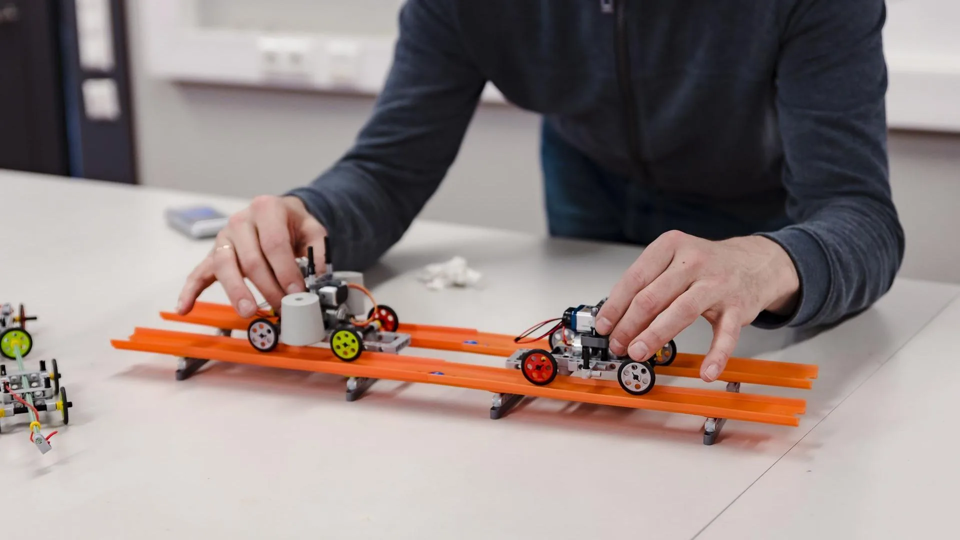 Small Praktikal experiment cars on an orange test track.